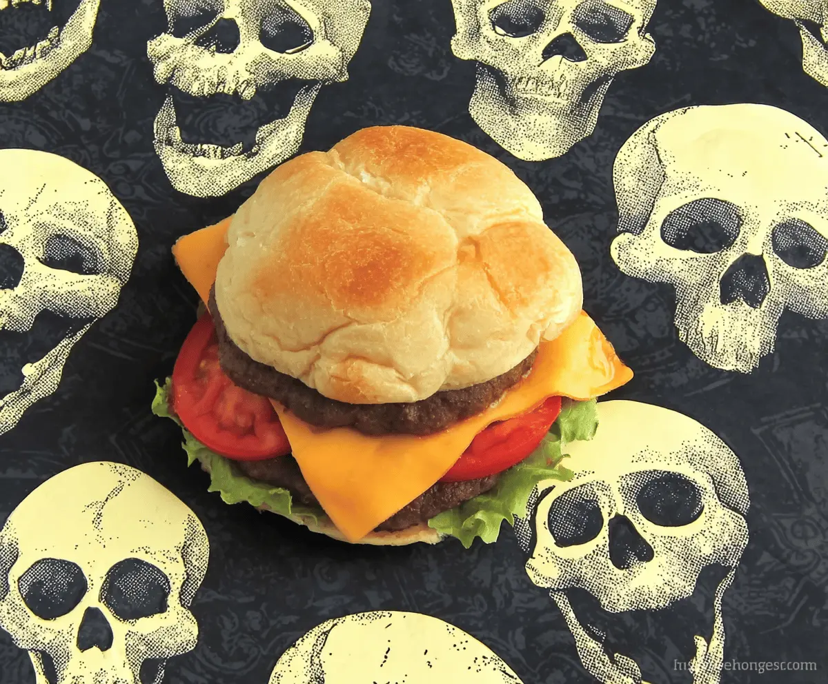 Delicious Cheeseburger Skulls featuring juicy beef patties, melted cheese, crispy bacon, fresh lettuce, tomato slices, and toasted buns shaped like skulls for a fun Halloween-themed appetizer.
