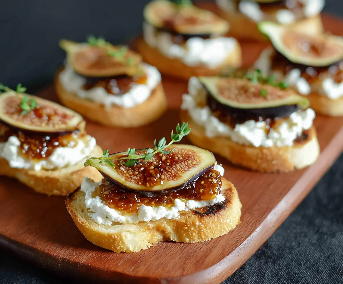 Delicious Fig Jam Goat Cheese Crostini garnished with fresh herbs on a wooden platter.