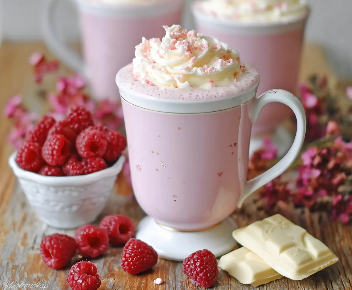 Delicious raspberry white hot chocolate in a cozy mug topped with whipped cream and fresh raspberries.