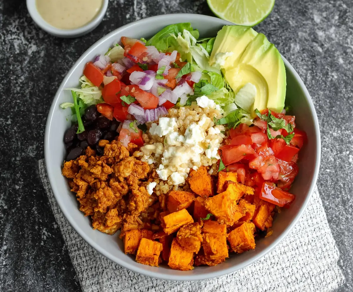 Colorful sweet potato taco bowls topped with fresh cilantro and shredded cheese, served in a rustic bowl.