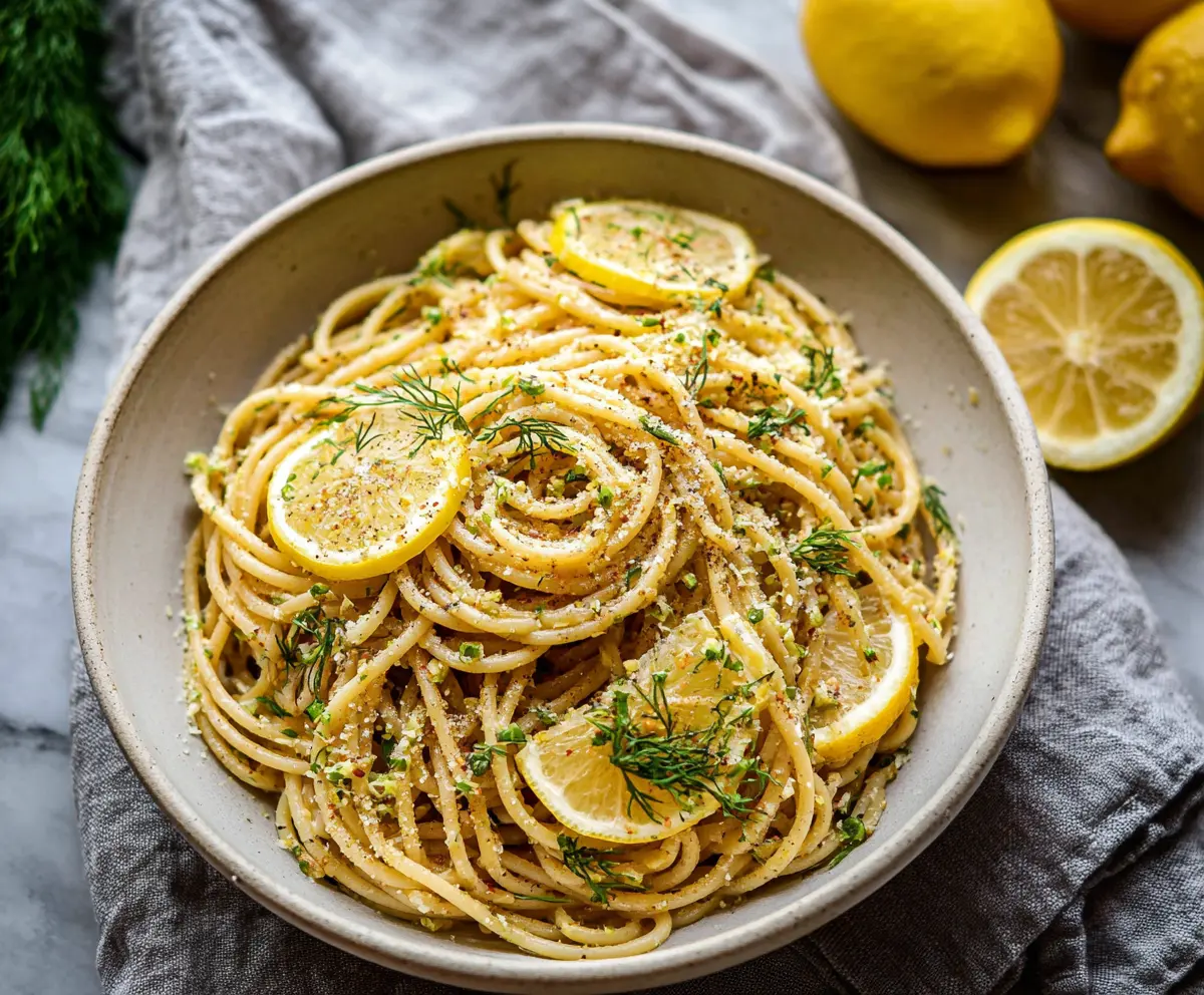 Close-up of browned butter lemon dill pasta served in a white bowl, garnished with fresh dill and lemon slices.